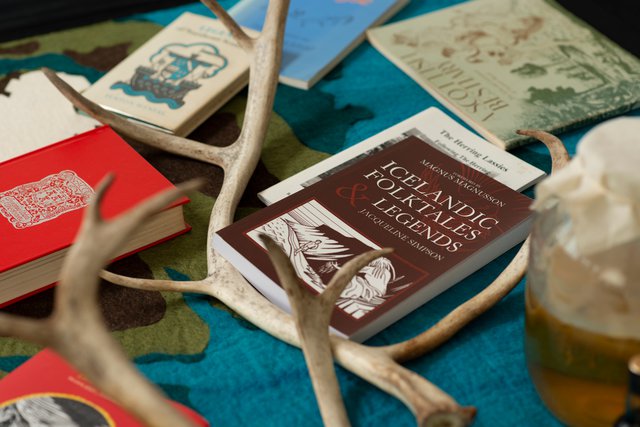 Detail photograph showing various books jumbled with reindeer antlers and a glass fermenting jar lying on a felt rug.